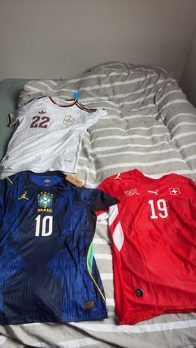 Un client montre son maillot bleu du Brésil Extérieur 2026 posé sur un lit à côté de deux autres maillots de football.