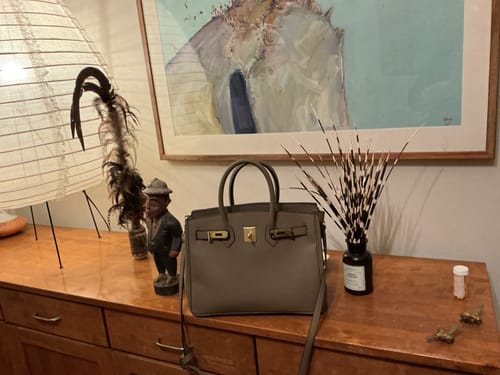 A reviewer's gray, structured Warkin Bag with gold hardware, sitting on a wooden dresser.