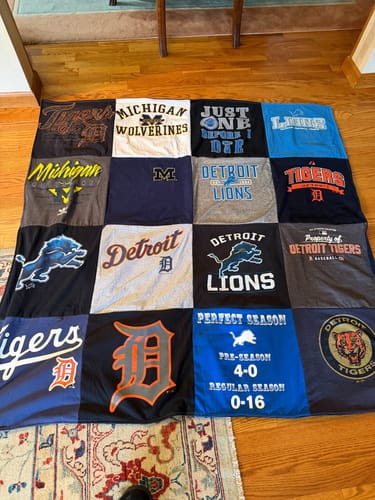 Customer's memorial Project Repat T-Shirt Quilt with Detroit sports team shirts spread out on a wooden floor.