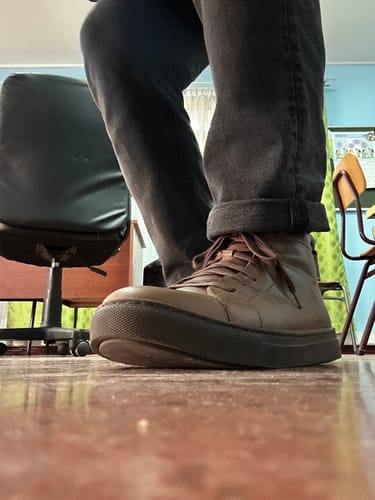 Primer plano de un cliente usando las zapatillas Berlin Chocolate con pantalones oscuros en un interior.