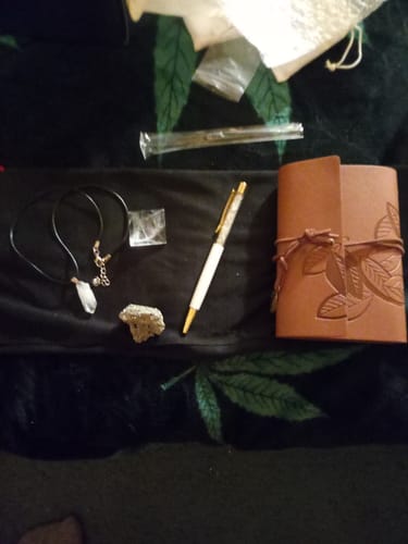 Reviewer's AuraBloom Subscription Box contents laid out, including a journal, a clear quartz pen, and several crystals.