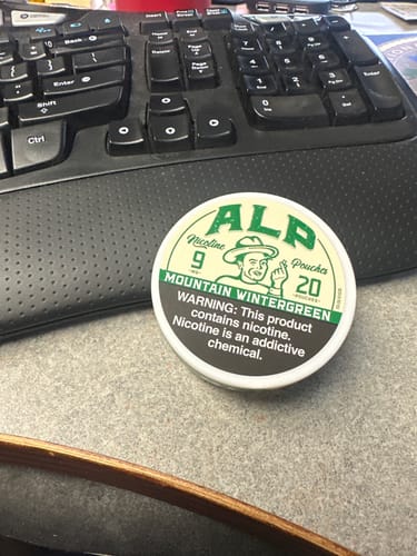 Customer's white tin of Mountain Wintergreen Nicotine Pouches resting on a desk.