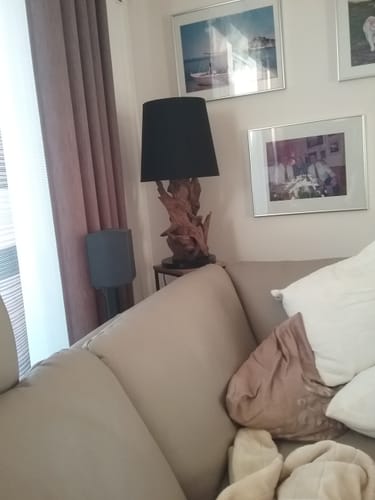 Kunde zeigt die Wurzeltischlampe mit schwarzem Schirm in einer Wohnzimmerecke neben einem Sofa.