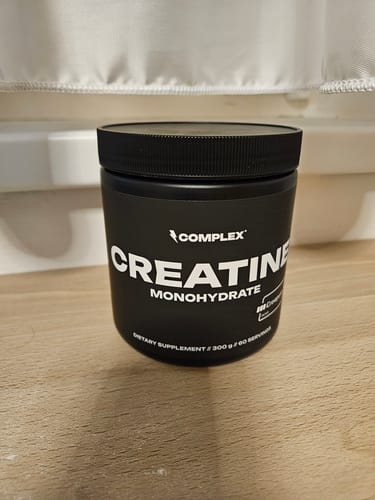 Customer's black tub of Complex Creatine Monohydrate supplement sitting on a wooden table.