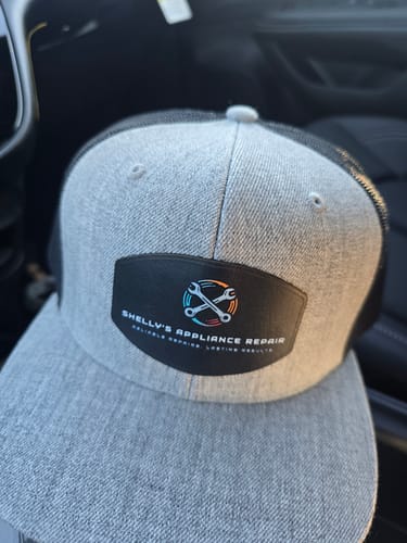 A customer's heather grey and black trucker hat with a custom full-color leather patch logo on the front.