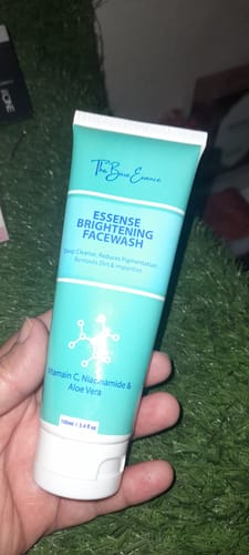 A customer's hand holds the teal tube of Essense Brightening Facewash.