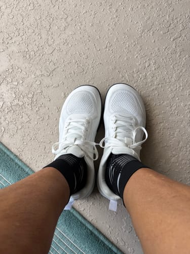 A reviewer's top-down view of their new white CUURT Muuv shoes on their feet.