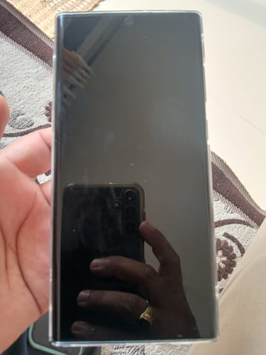 Reviewer holding a smartphone with the UltraShield Tempered Glass installed, showing its clear and reflective surface.