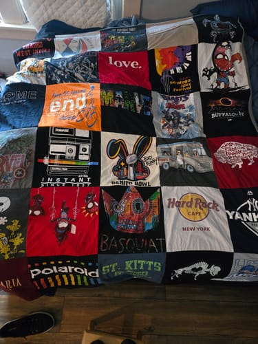 Customer's large, colorful Project Repat T-Shirt Quilt made from various graphic t-shirts and spread over a bed.
