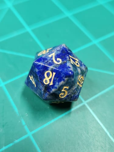 Customer's blue gemstone URWizards D20 dice with gold numbers shown on a green cutting mat.