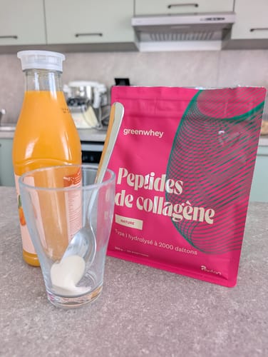 Un client prépare ses Peptides de Collagène. La poudre est dans un verre à côté du sachet rose et d'un jus de fruits.