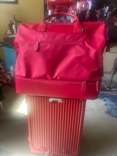 Customer's red weekender bag shown sitting on top of a red rolling suitcase.
