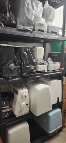 A customer's collection of sewing machines and carrying cases organized on black storage shelves.