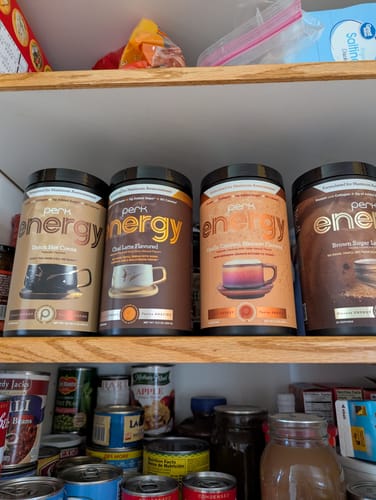 Reviewer's Perk Energy Chai Latte container on a pantry shelf with other flavors from the brand.