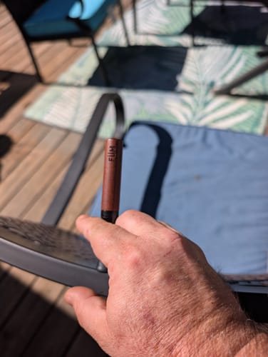A customer's hand holding the brown Füm device while sitting outside on a sunny patio.