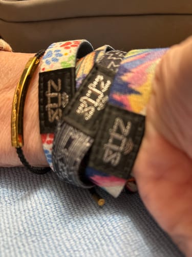 Customer's wrist showing the paw-print Always By Your Side Bracelet worn in a stack with other colorful fabric bracelets.