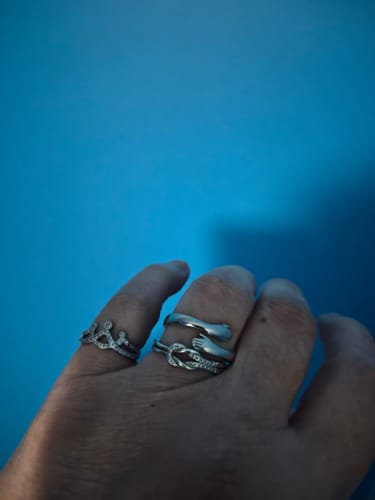 Customer's hand wearing the Straighten Your Crown Ring on the index finger, alongside two other silver rings against a blue background.