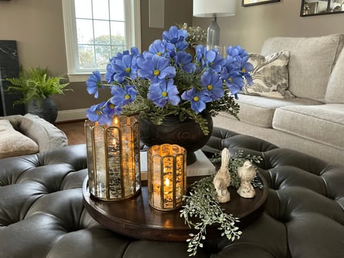 Reviewer's vibrant Faux Blue Cosmo Stems arranged in a dark wood vessel on a living room ottoman.