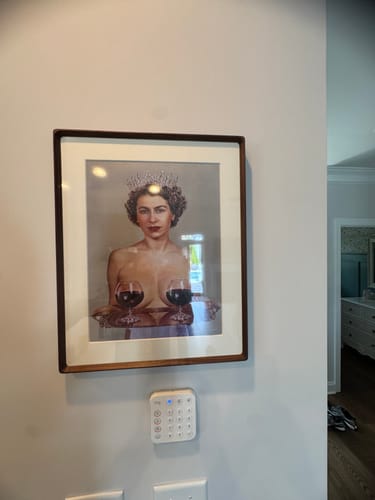 Reviewer's framed Majestic art print on a wall, depicting a crowned woman with wine glasses for breasts.