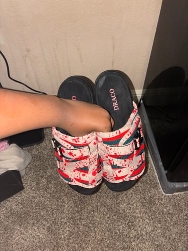 Customer holding a pair of Nightmare DracoSlides, showing the red and green splatter-patterned straps.
