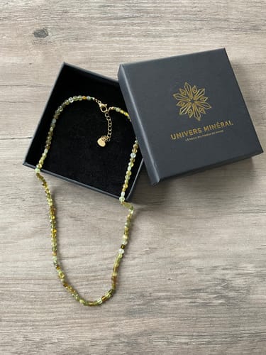 Le collier en Grenat Vert d'un client, avec ses perles facettées, posé à côté de son écrin noir.
