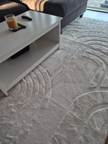 Customer's cream Mellow Mat with a soft, carved pattern laid out in a living room next to a sofa.