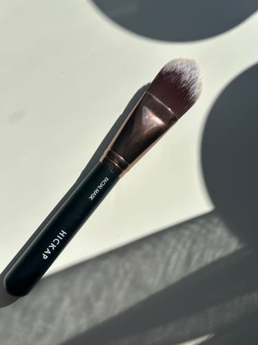 Kundens ansiktsmaskborste med ett svart handtag och roséguldfärgad hylsa, liggande på en ljus yta.