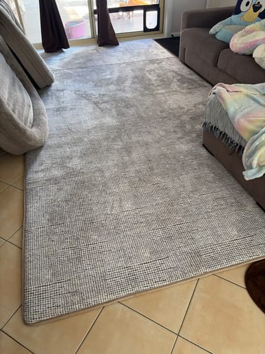 Customer's large pebble-weave Mellow Mat laid out on the tiled floor of a living room in front of a sofa.