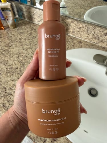 Customer holding the Accelerating Tanning Bundle oil and moisturiser in a bathroom.