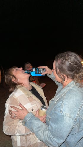 Reviewer pours the blue Blue Rasp 700ml drink from the bottle into another person's mouth outdoors.