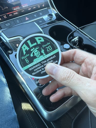 Customer holding a round tin of Refreshing Chill Nicotine Pouches in a car.