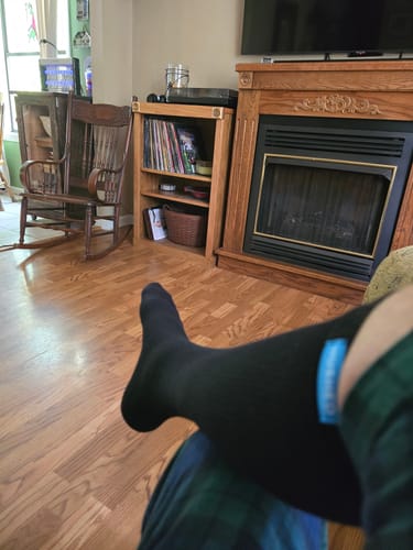Customer's leg and foot wearing a black Performance Eucalyptus Compression Sock in a living room.