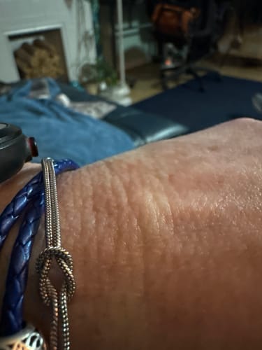 Close-up of a reviewer's wrist wearing a silver-colored knot bracelet and a blue braided bracelet.
