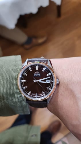 Cliente mostrando su reloj Orient Automatic en la muñeca, con una esfera marrón y bisel en tono oro rosa.