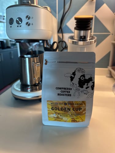 Customer's bag of Golden Cup Blend coffee on a kitchen counter next to a white espresso machine and grinder.