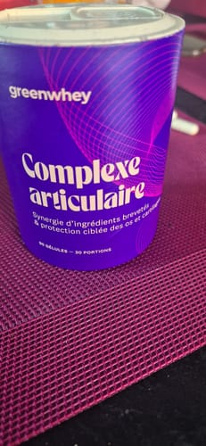 Client montrant le pot violet du produit Complexe Articulaire Greenwhey sur un set de table.