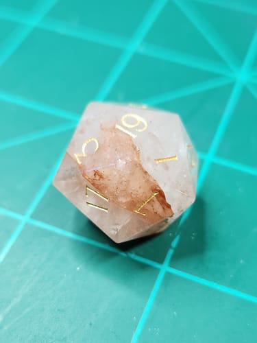 Close-up of a reviewer's Fire Quartz d20 die, showing the internal red inclusions and gold engraved numbers.