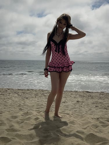 Reviewer wearing the pink 1940s halter polka dot one-piece swimsuit on a sandy beach.