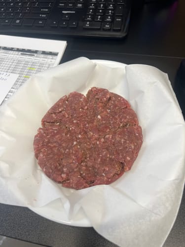 Customer showing a large, raw patty of Grass Fed Ground Beef on a plate lined with paper.