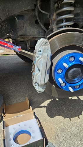 Customer's blue hubcentric wheel spacer installed on a vehicle's wheel hub, with the open product box visible on the ground.