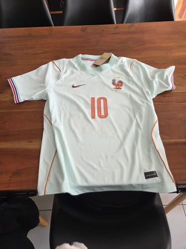 Photo d'un client montrant le maillot France Extérieur 2026. De couleur claire avec le numéro 10, il est posé sur une table.