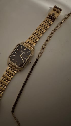 Customer's Jade Gold Burgundy Bracelet laid out on a flat surface next to a gold watch.