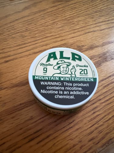 Reviewer's can of ALP Mountain Wintergreen nicotine pouches sitting on a wooden surface.