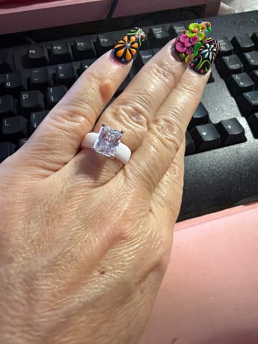 A reviewer's hand showing the Silicone Ring, which has a white band and a large, emerald-cut stone.
