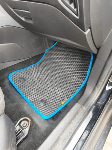 Klienta czarny dywanik samochodowy z niebieską lamówką, idealnie dopasowany w miejscu pasażera.