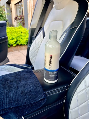 Reviewer's Leather Cleaner bottle on a car console next to a clean, two-tone leather seat.