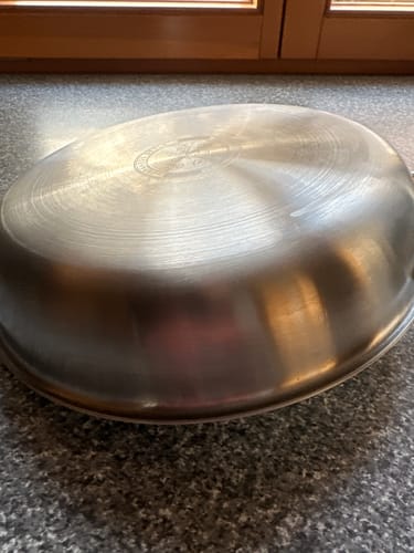 Rezensent zeigt den Boden der umgedrehten Titanpfanne, der laut Bewertung nicht flach ist.