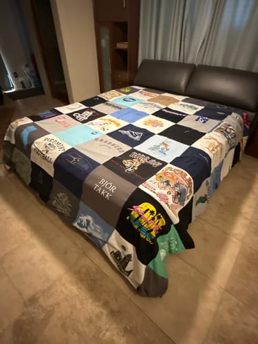 Reviewer's large, colorful Project Repat T-Shirt Quilt spread neatly across a bed in a bedroom.