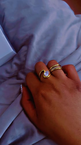Customer's hand resting on a grey cloth, wearing the gold Naya Ring with its sculptural band and single stone.