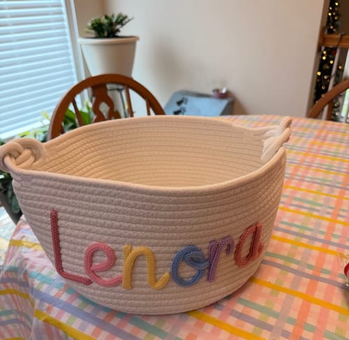 Customer's personalized knitted basket with the name 'Lenora' in multicolor yarn, sitting on a table.